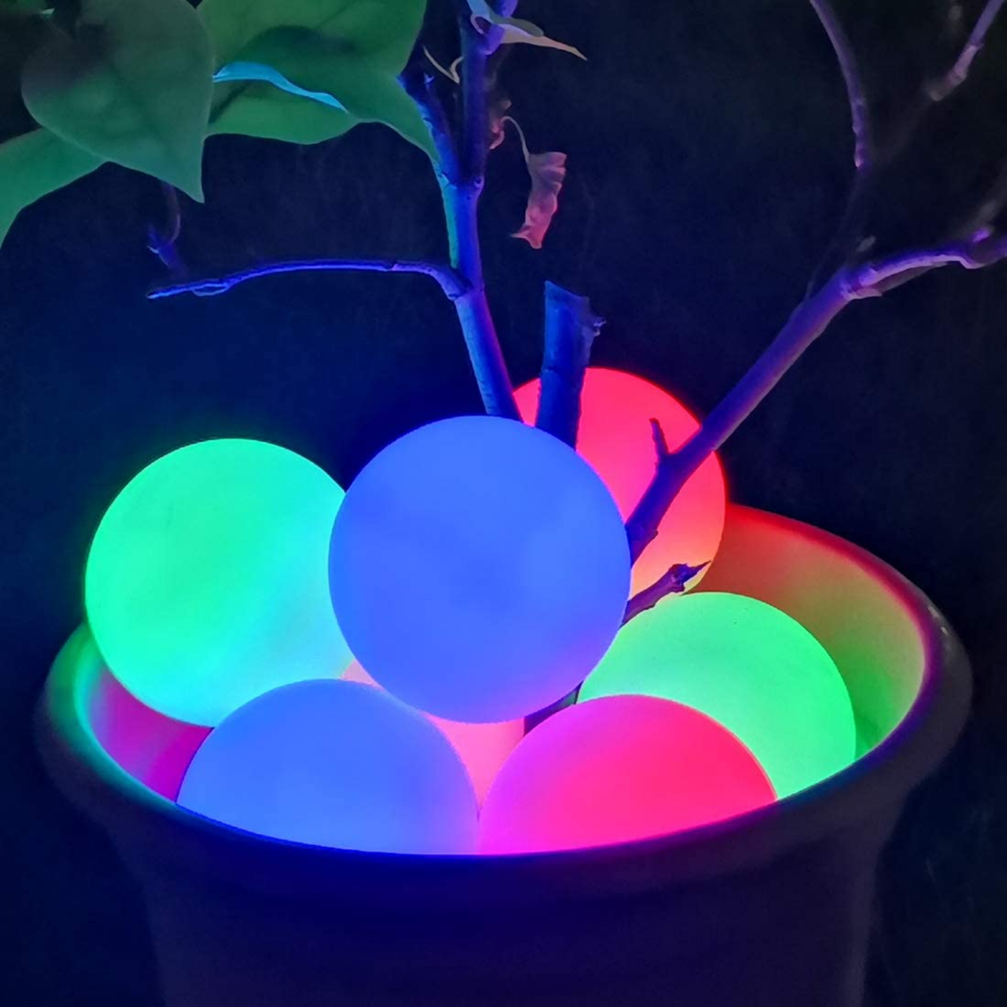 Sensorii's light up toys- 6 of Sensorii's light-up waterproof balls, 2 are green, 2 are blue, and 2 are red. The 6 balls are lit up in the dark and placed in a large plant pot